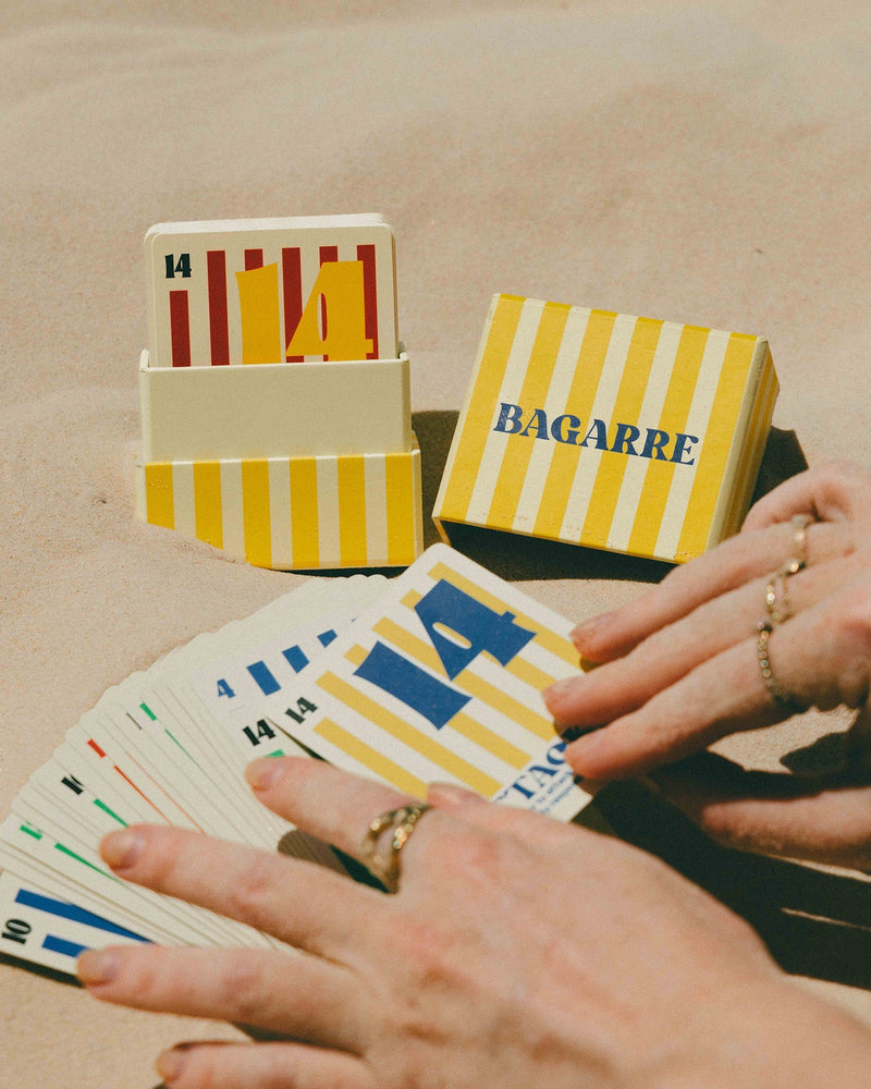 Playing cards with yellow and white striped box labeled 'Bagarre' on a sandy background